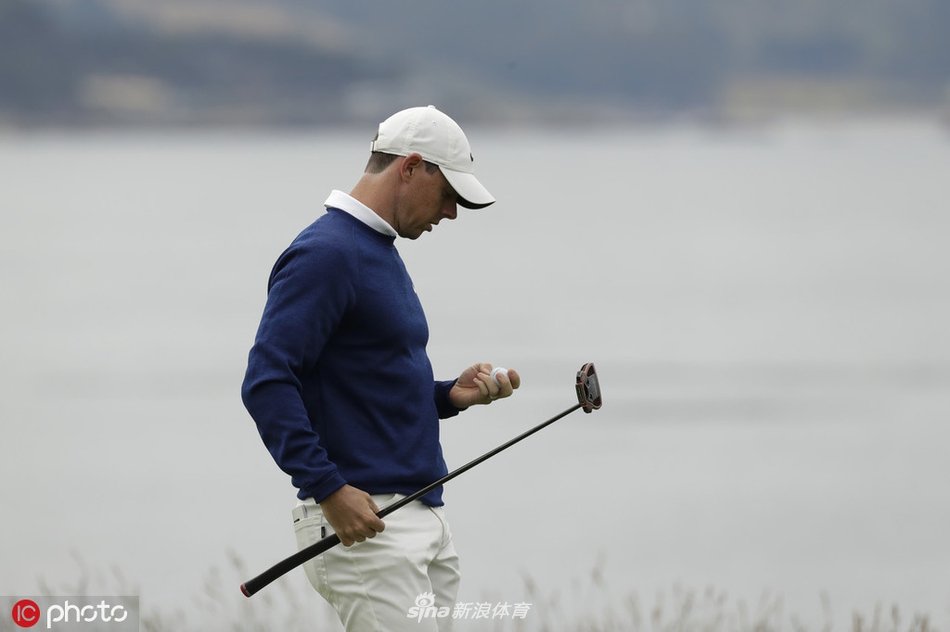 罗里·麦克罗伊在圆石滩球道上专注地审视攻果岭线路,海风吹动他的衣角,身后是波澜壮阔的太平洋景象。