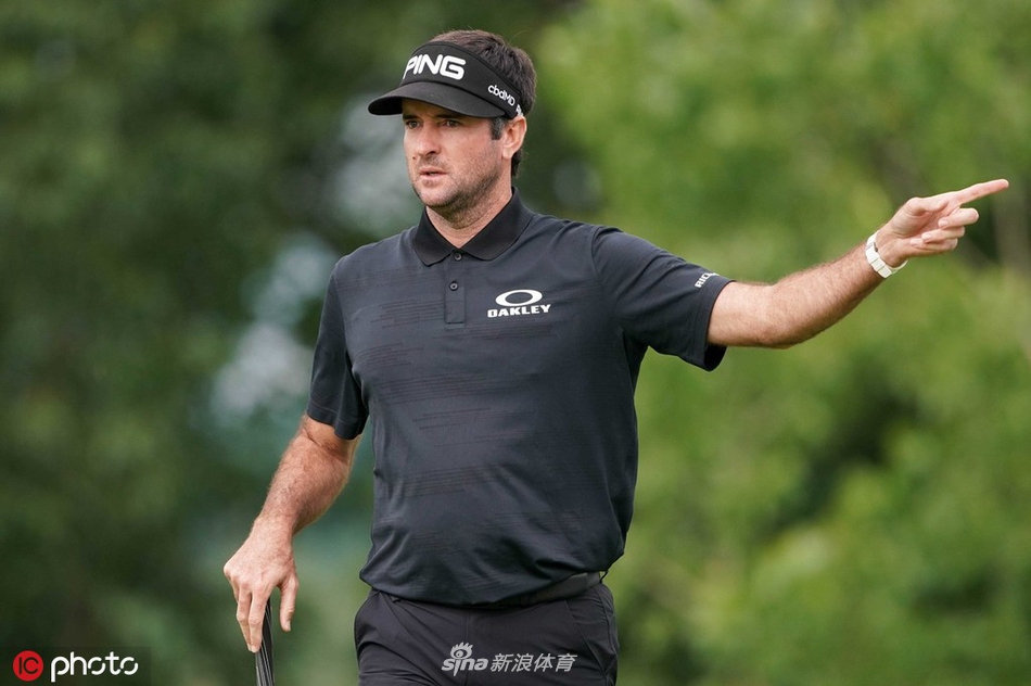 旅行者锦标赛次轮比赛全景，蜿蜒的球道与碧绿的果岭在夏日的阳光下延伸，球员与观众的身影点缀其间，构成一幅优美的高尔夫画卷。