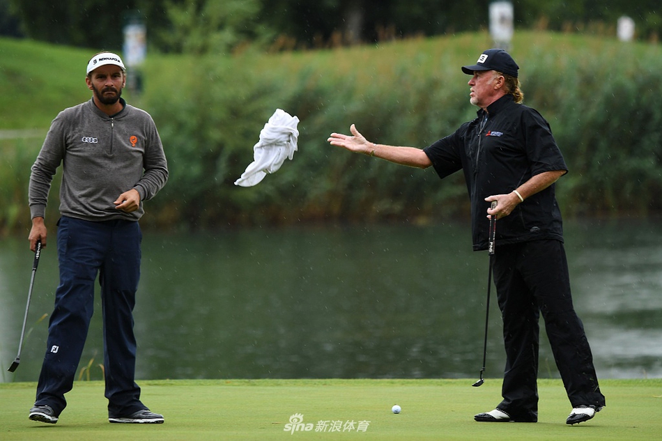 高尔夫球浸泡在果岭边积水的小坑中，水面倒映着灰暗的天空，生动展现了比赛面临的极端场地状况。