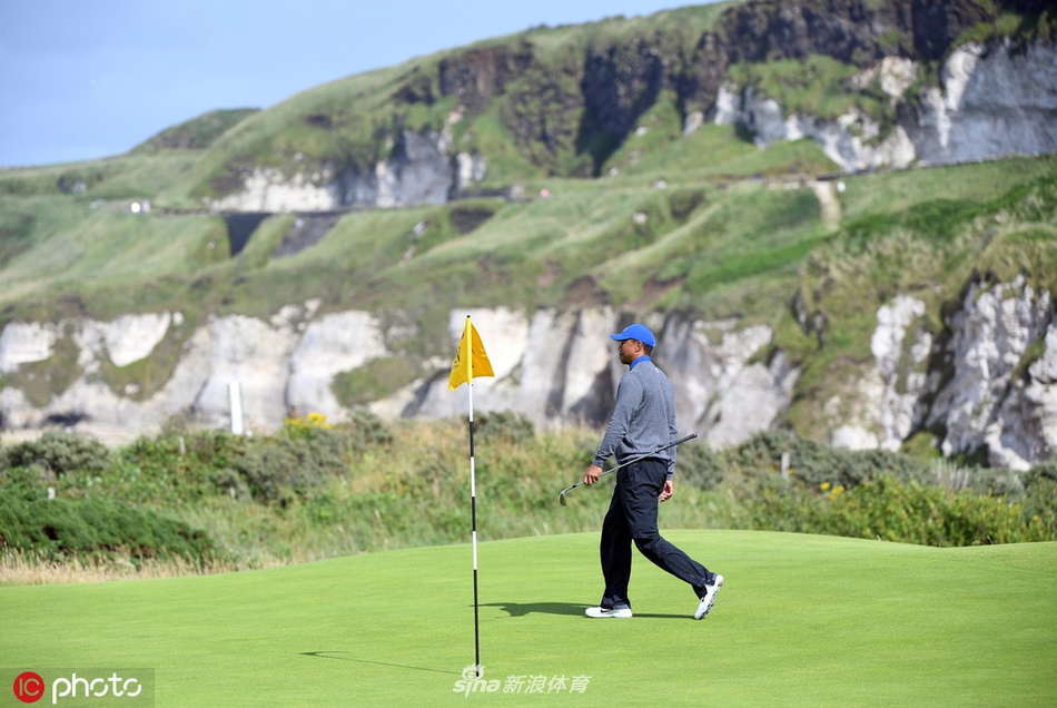 泰格·伍兹在冷雨中凝神准备开球,他身着灰色毛衣与黑色雨裤,面庞在风雨中显得格外坚毅又略带凝重。