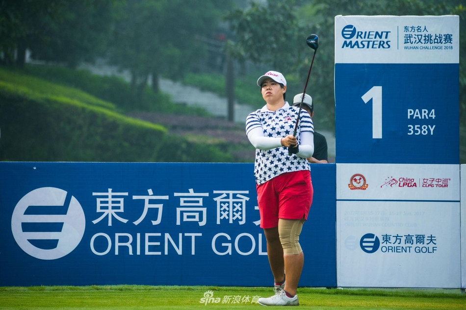 赛事志愿者手持记分牌，背景是郁郁葱葱的树林与晴朗天空