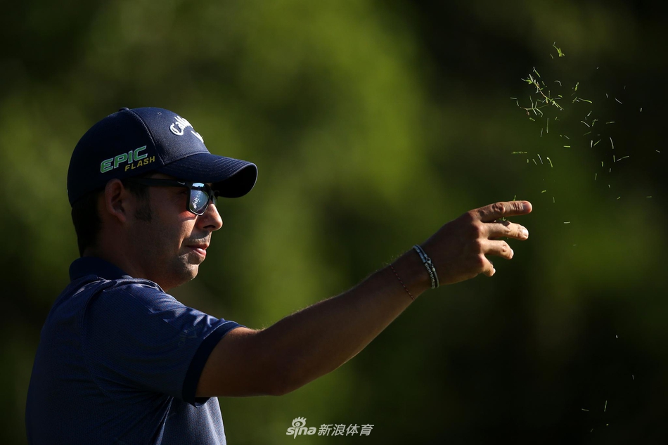 拉拉扎巴尔在果岭边细致观察推杆线路,神情专注,背景是广阔的球场与蓝天。