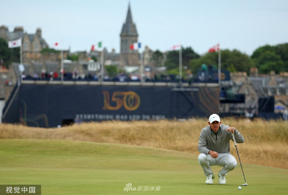 罗里·麦克罗伊在第十洞沙坑中准备击球，神情专注，身后是古老的圣安德鲁斯球场和屏息期待的观众。