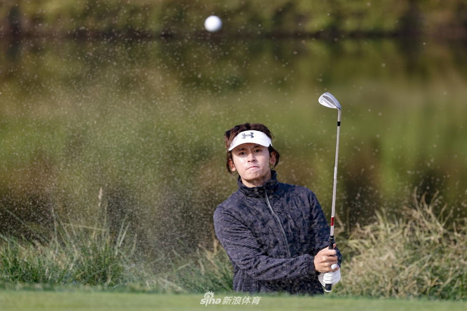 张哲瀚凝神静气，正以标准姿势进行切杆练习，白色球帽下目光如炬，全然沉浸在高尔夫运动的技巧世界中。