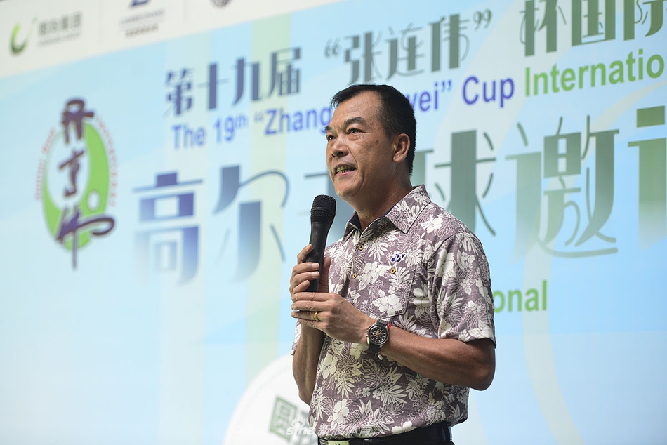 张连伟先生面带笑容,亲身指导一位小球员挥杆,背景是绿意盎然的高尔夫练习场,展现了薪火相传的温暖瞬间。