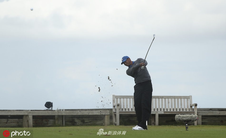 伍兹在风雨中独自走向下一个发球台,背影显得有些孤独但依然挺拔,雨滴在空中划出细密的线条,勾勒出高尔夫球员最经典的坚韧形象。