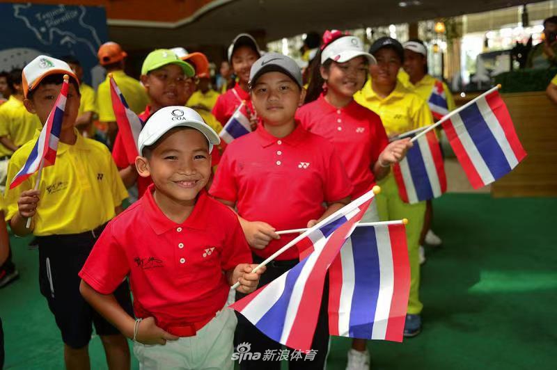 亲子配对赛中,一位父亲正微笑着看向自己的孩子,孩子则专注地摆弄着手中的高尔夫球,画面充满安静而亲昵的互动感。