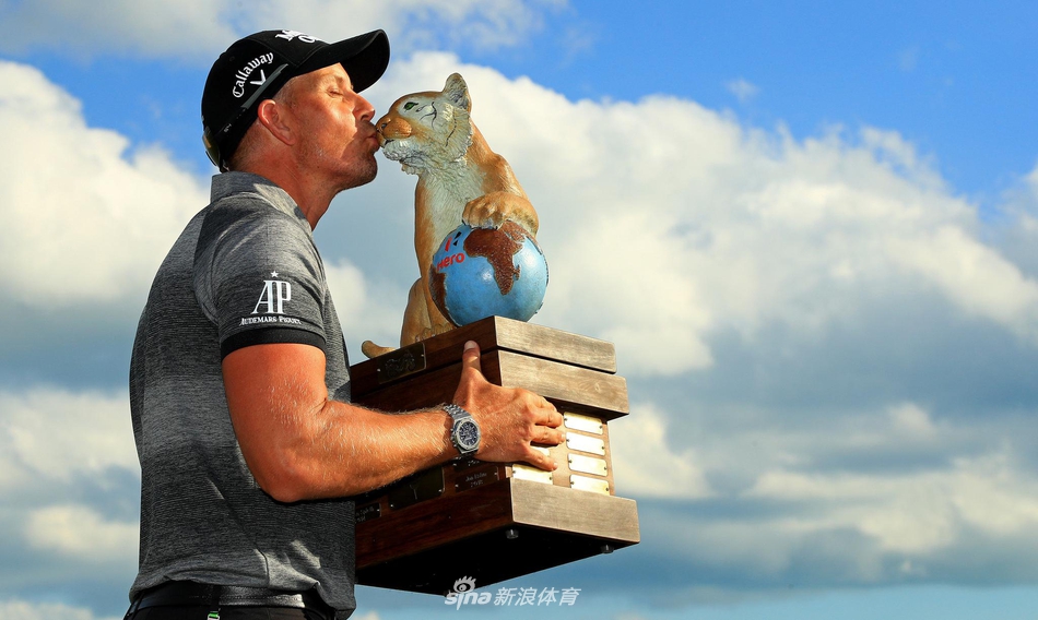 冠军斯滕森面带笑容高举奖杯，背景是碧海蓝天与阿尔巴尼球场的沙丘景观