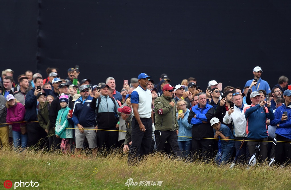 伍兹完成一记推杆后抬头看线,眼神中充满了对球路的期待与一丝不易察觉的疲惫,背景是北爱尔兰典型的阴沉天空与广阔球场。