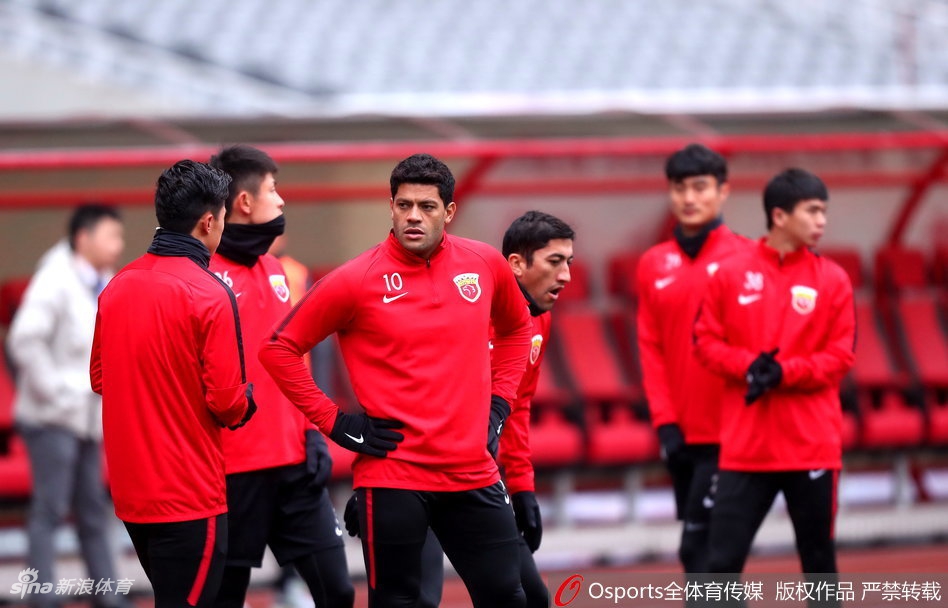 上海上港众将身着红衣在雨雾缭绕的上海体育场进行赛前最后一练，球场灯光映照下，草皮显得格外翠绿，球员神情专注，大战一触即发。