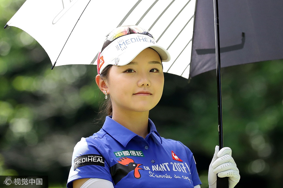 石昱婷在雨中撑着高尔夫球伞，全神贯注地观察果岭推杆线路，眼神沉着而坚定。