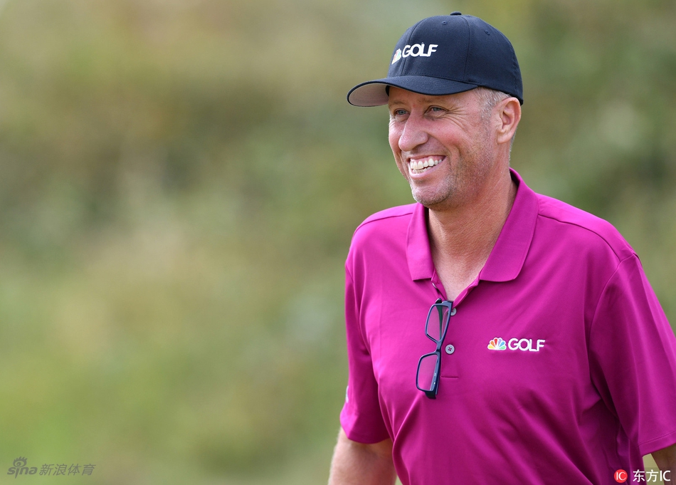 传奇球童麦克凯手持麦克风，在皇家伯克戴尔球场边进行赛前准备，专注地审视着眼前的挑战性球道。