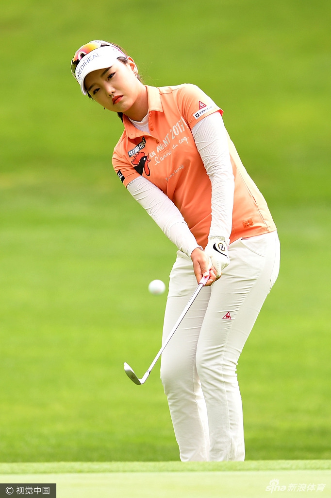 石昱婷完成击球后，手持球杆自信地走向果岭，背景是郁郁葱葱的球场树木