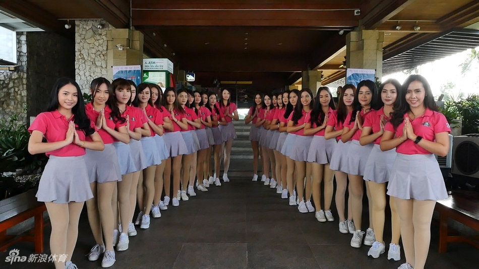 身着传统泰式服装的球童在球道上撑伞，笑容温婉，与绿茵球场构成和谐画面。