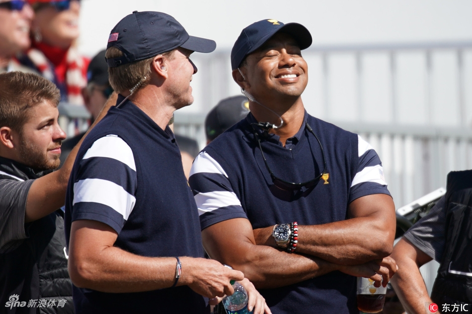 泰格·伍兹身穿美国队制服，环抱双臂站立在赛场边，神情轻松而专注，展现出作为团队领袖的沉稳气场。