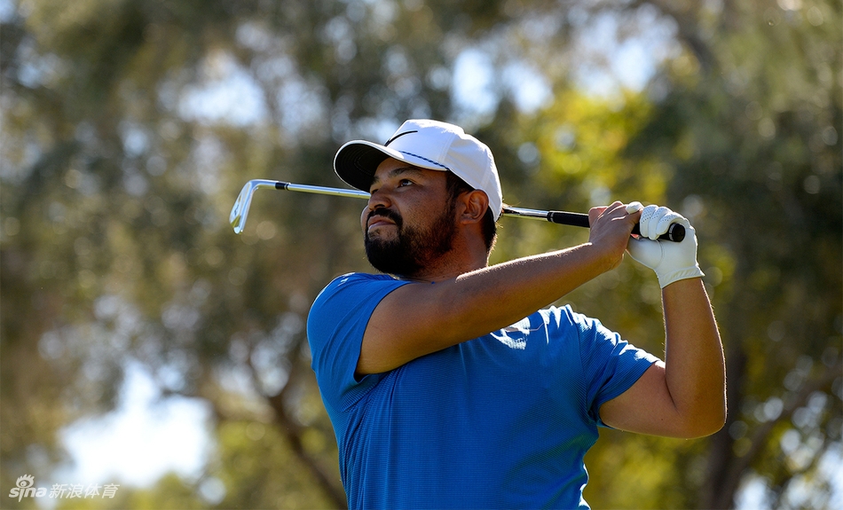 J.J.斯鲍在球道沙坑中救球，表情专注，强风吹动了他的衣角和头发，生动展现了比赛日的艰难条件。