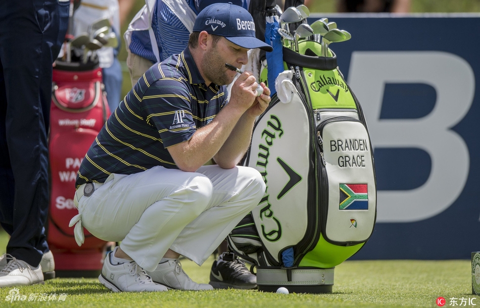 斯科特·杰米森在太阳城球场果岭边凝神观察推杆线路，阳光为他专注的身影勾勒出金色轮廓