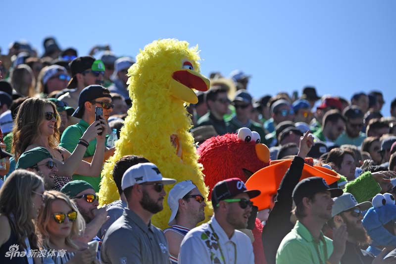 四位笑容灿烂的年轻女性观众并肩站在看台前，她们分别穿着红、白、蓝等鲜艳颜色的休闲装，背后的赛场旗帜在微风中飘扬，洋溢着青春的活力。