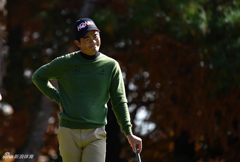 梁文冲与球童在果岭边蹲身认真研讨推杆线路，两人神情专注，共同应对比赛挑战