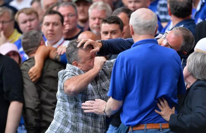 冲突被周围球迷拉开，一名身穿灰色卫衣的男子努力隔开两人，而打红眼的其中一方仍试图挣脱，手臂青筋暴起。