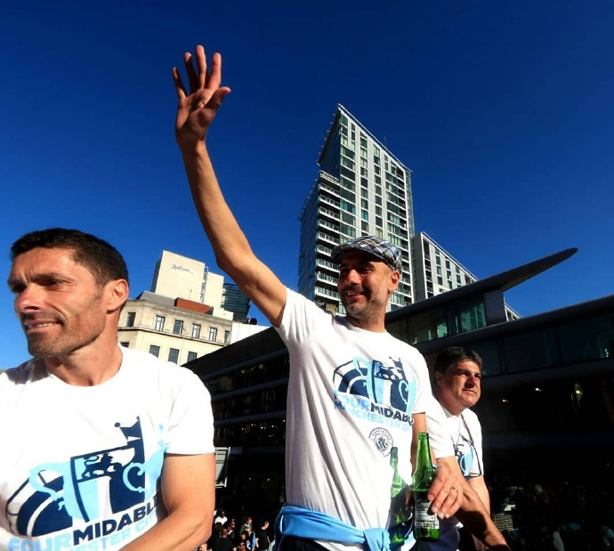 曼城球员们在巡游大巴上，簇拥着闪闪发光的英超冠军奖杯，五彩的纸屑在空中飘洒，映衬着每个人脸上的灿烂笑容。