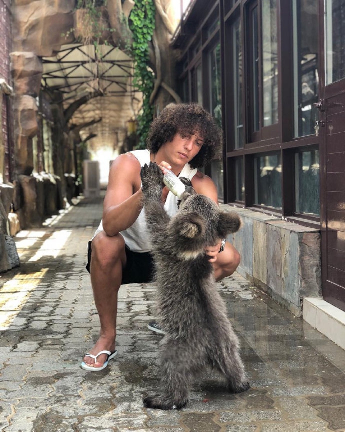 高大的长颈鹿低下头，伸出长长的舌头，亲昵地舔向大卫-路易斯的脸颊。路易斯被这突然的举动逗得既惊讶又开心，脸上浮现出经典的呆萌笑容。