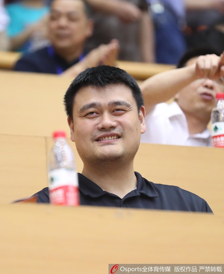 姚明坐在场边，神情略显无奈又带着一丝宠溺的笑容，仿佛在说这帮孩子打得真是让人又爱又急