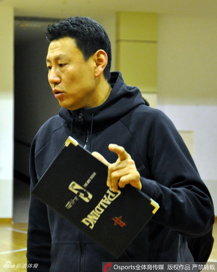 主教练李楠指导双手叉腰站在场边，目光如炬地注视着场内训练，神情专注，随时准备叫停纠正球员的技术动作。