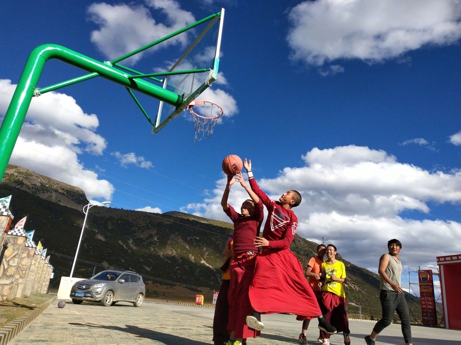 在高原湛蓝的天空下,一位身着绛红僧袍的喇嘛高高跃起,手中的篮球仿佛要挣脱地心引力,他的身影在简陋的篮球架前显得格外轻盈而专注。