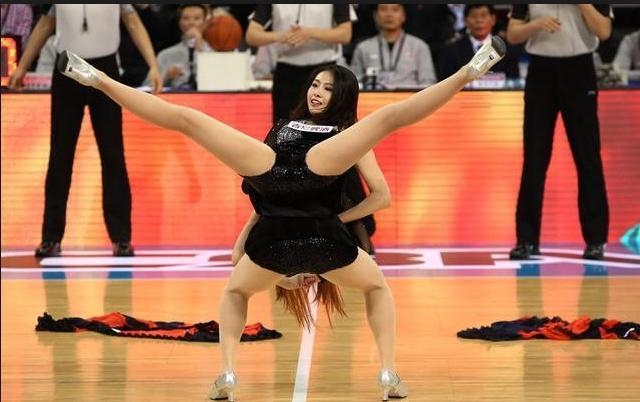 一位篮球宝贝在完成一字马动作后，低头微笑，眼神温柔而充满感染力，她身后的队友们还在尽情舞动，整个画面定格了活力与柔美的完美结合，让人感受到篮球宝贝的热情。