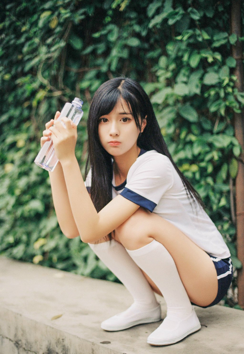 她双手轻托脸颊,眼中映出绿色草坪的光影,嘴角带着少女般俏皮的笑意,青春气息扑面而来。