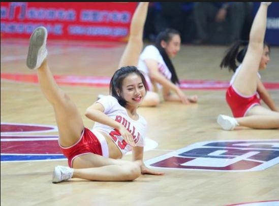 近景镜头下，一位篮球宝贝正在侧身展示一字马，优美的身体线条和紧绷的脚尖，显示出深厚的舞蹈功底，背景是模糊的观众席，仿佛整个赛场都在为她的专注而静止。