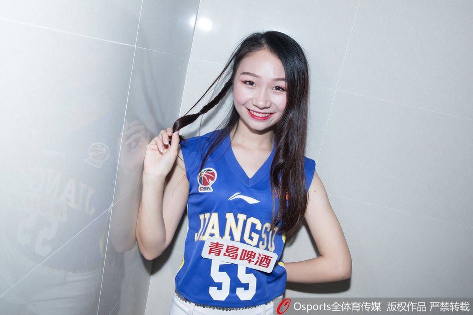 写真中，一位KDancer成员坐在更衣室的储物柜旁，单手托腮，眼神温柔而坚定，修长的身形在暖黄色的灯光下勾勒出迷人的轮廓，美得如同一幅油画。