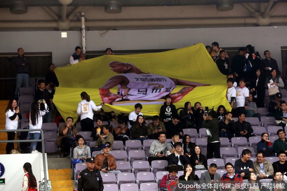 比赛进入白热化阶段，马布里在弧顶持球观察队友跑位，身后的看台上，他那幅巨大的黑白肖像海报如同守护神一般俯瞰着全场，与看台上涌动的人潮构成了一幅令人动容的画卷。