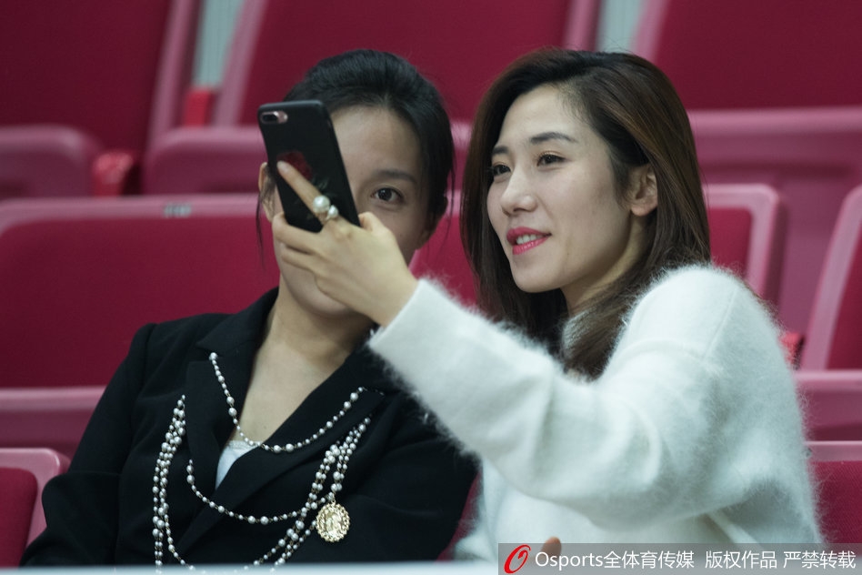 这位女球迷身穿简约的休闲装，正与身边的同伴交流着场上的形势，嘴角带着一丝自信的微笑，仿佛早已看穿了接下来的战术。