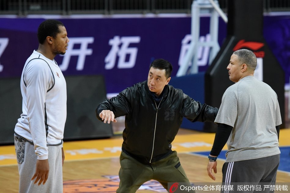 训练结束后，休利与王非在场边促膝长谈，两人面带笑容，身后的球馆灯光映照着这份深厚的篮球情谊。