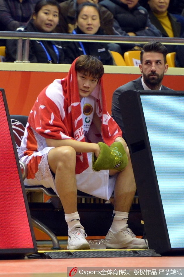 小丁抱着篮球在更衣室，歪着头看着镜头，脸上挂着腼腆而温暖的笑容。