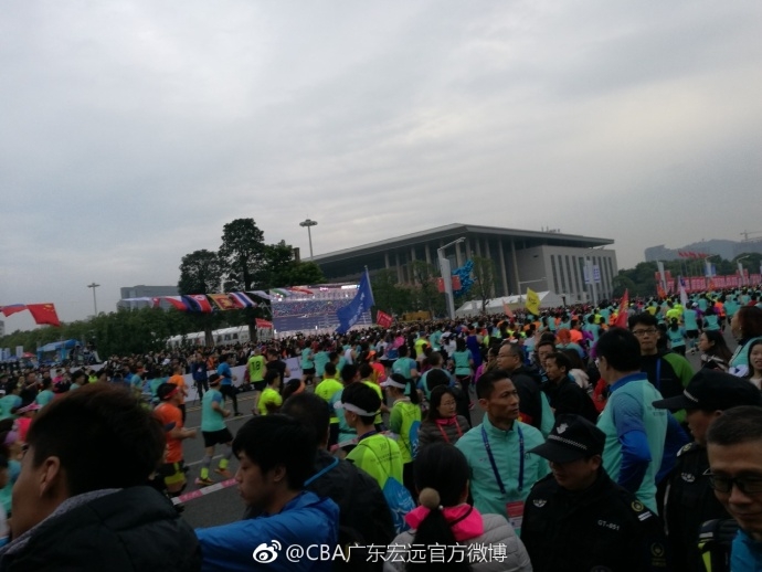 身着厚实外套的广东队明星球员易建联，在东莞清晨的微光中现身马拉松起跑点，他标志性的笑容如同暖阳，瞬间驱散了南国冬日的寒意，引来周围跑友惊喜的目光。