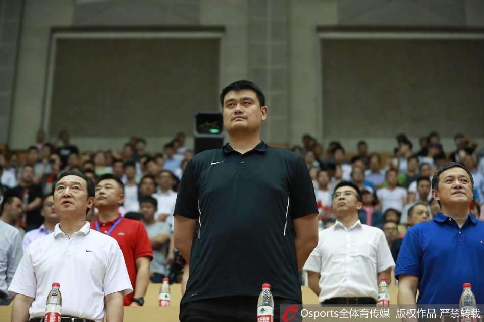 姚明与身旁的人交流，脸上露出一种高深莫测的微笑，似乎在传授什么篮球秘籍或者点评刚才的战术