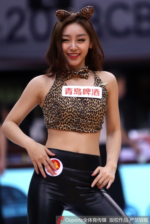 特写镜头中，一位啦啦队员长发飘逸，嘴角上扬露出迷人的微笑。紧身的豹纹皮裤勾勒出她修长的腿部线条，她高举手臂打着节拍，用热情洋溢的肢体语言带动着看台上球迷的助威声浪。