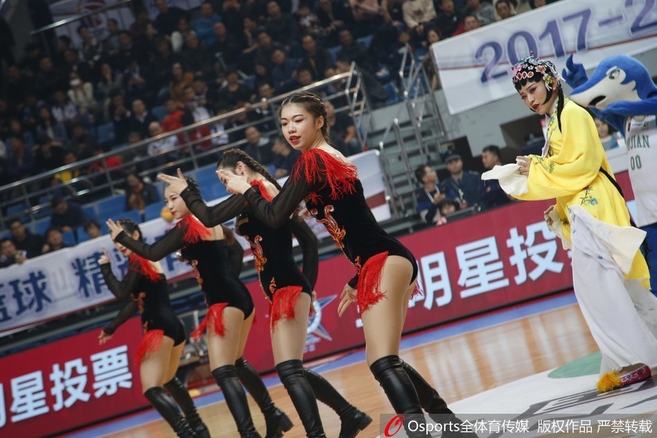 在激烈的比赛间隙，几名篮球宝贝聚在一起对着镜头挥手，她们的戏曲装扮与身后巨大的记分牌以及奔跑的球员形成动静皆宜的画面。