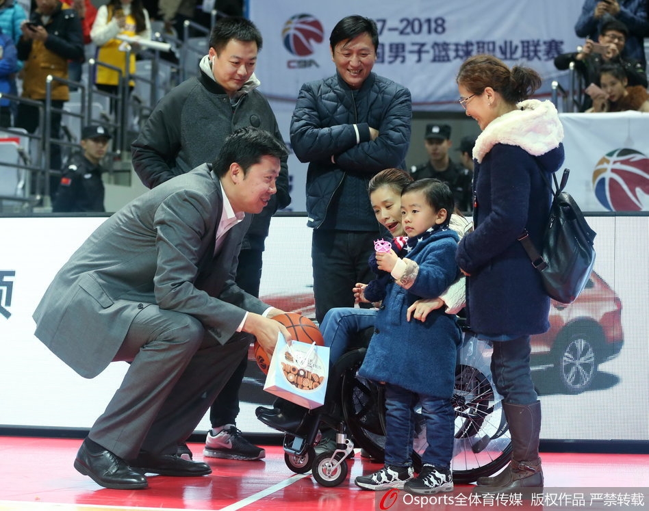 王治郅站在场边，正在给八一队的年轻球员布置战术，他的表情专注而认真，手里比划着跑位路线，身后的球馆灯光将他的身影拉得很长。