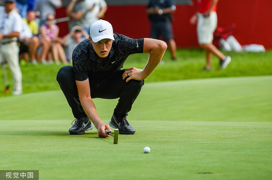 凯文-基斯纳在果岭上沉稳推杆，背景是宁静的湖泊和葱郁的树木，气氛紧张而肃穆。