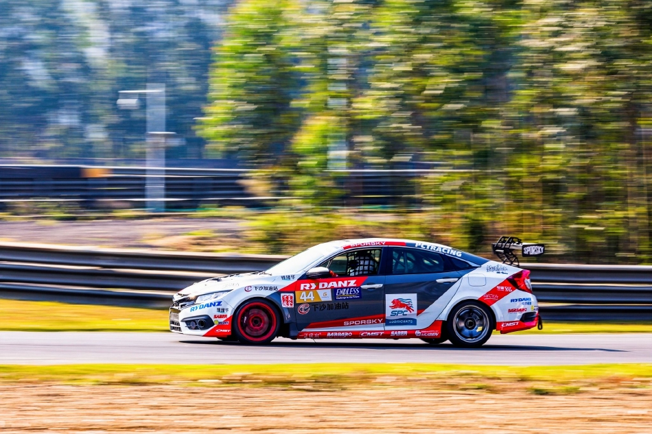 一辆蓝色赛车在弯心划出完美的弧线，车身拉出动态模糊，背景看台与树木飞速后退。