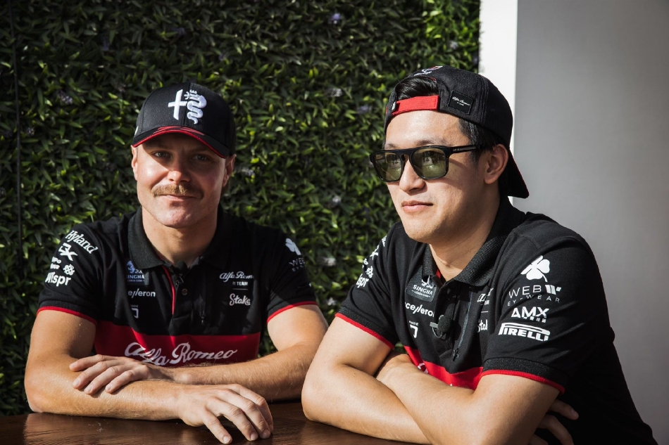 一位车手站在自己色彩鲜明的赛车旁,手扶座舱边缘,正侧耳倾听工程师的赛前简报,头盔下的眼神沉静而专注。