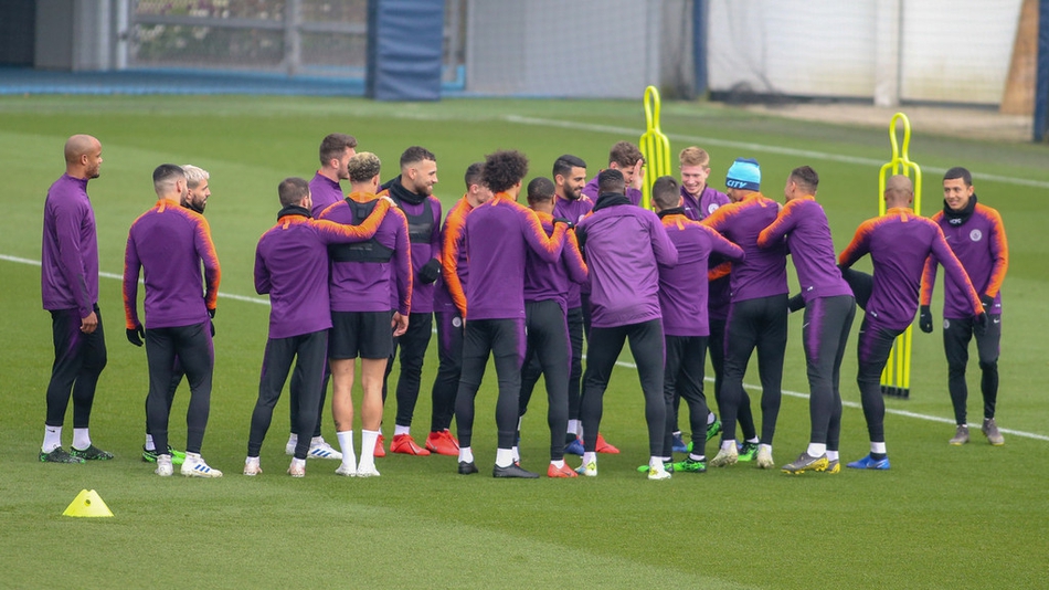 曼城全体球员在训练场上围成圆圈进行抢圈热身，阳光明媚，大家脸上洋溢着笑容，德布劳内一脚出球格外潇洒