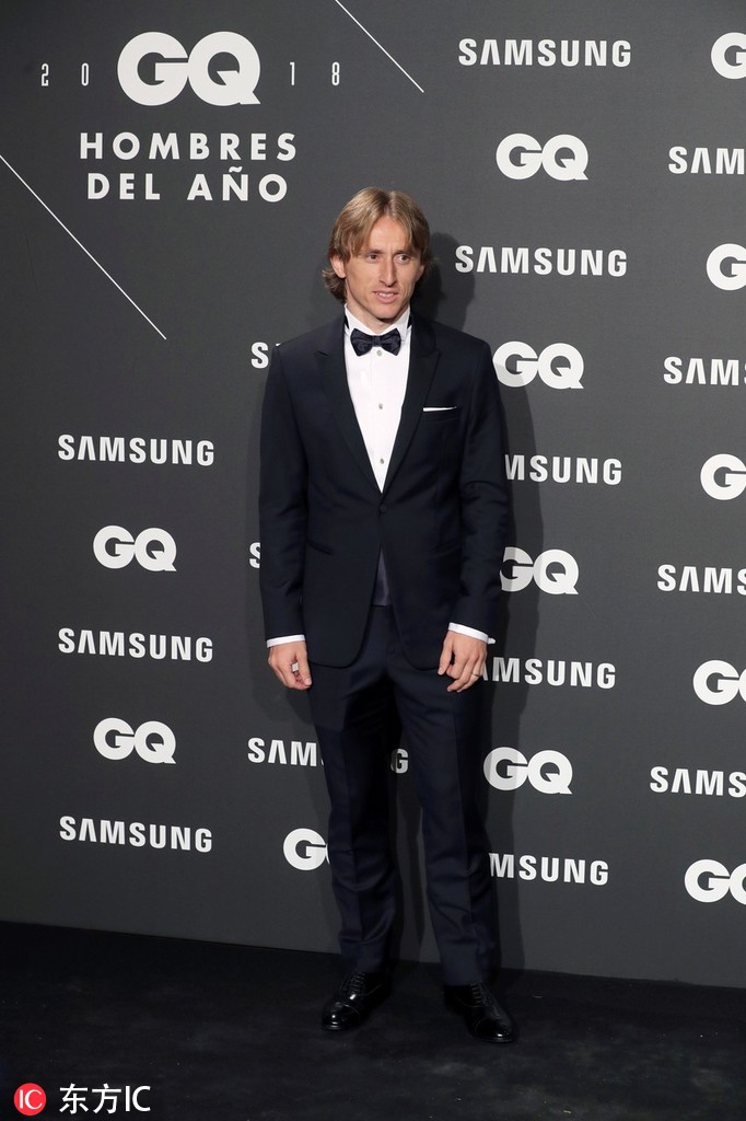 莫德里奇在颁奖台上发表感言，目光坚定而深邃，他身后的背景板上印着GQ的标志。他手持麦克风，正在分享自己职业生涯的心路历程，感谢家人与球队的支持，现场来宾报以热烈掌声。