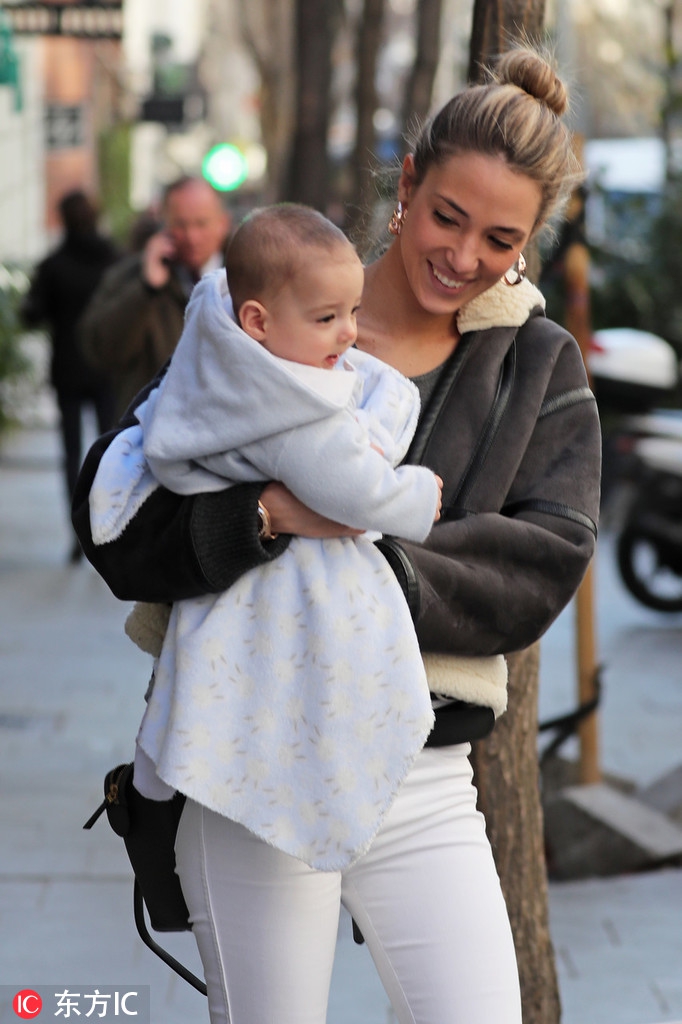 莫拉塔俯身查看婴儿车内的孩子，他穿着深色休闲裤显得身形修长，妻子在一旁温馨注视，一家四口其乐融融。