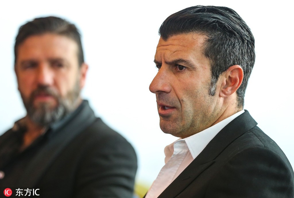 菲戈在论坛上单独发言，背景是巨大的论坛主题背板，他手持话筒目光坚定，仿佛正在向年轻一代传授关于边路突破的艺术与智慧