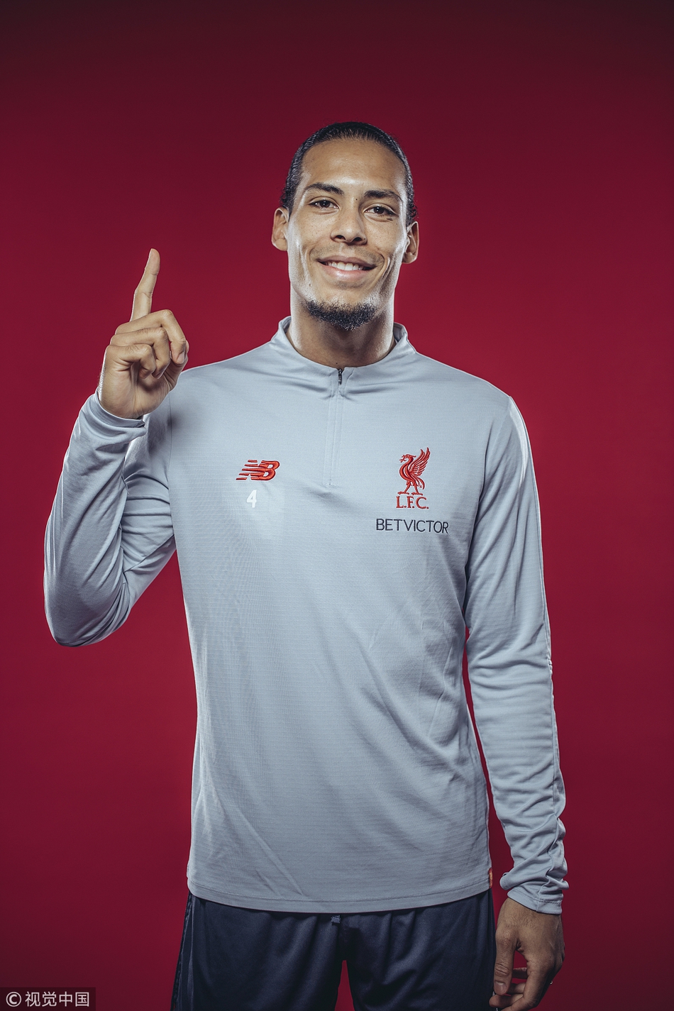 范迪克双手叉腰站立，身姿挺拔如松，红色的训练服在绿茵场映衬下格外醒目，尽显世界顶级中卫的自信与风范。